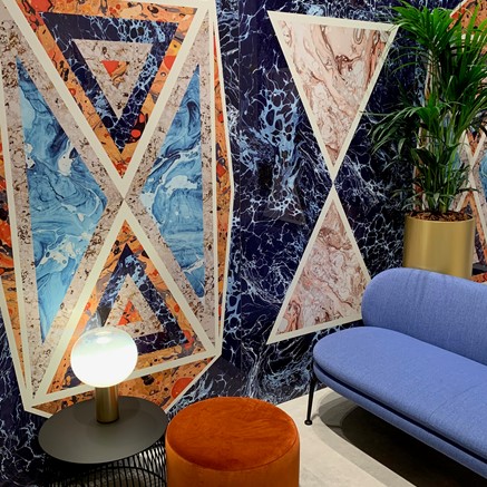 Interieur met blauwe zetel, roestkleurige poef, bijzettafel en plant met een kleurrijke tegelmuur